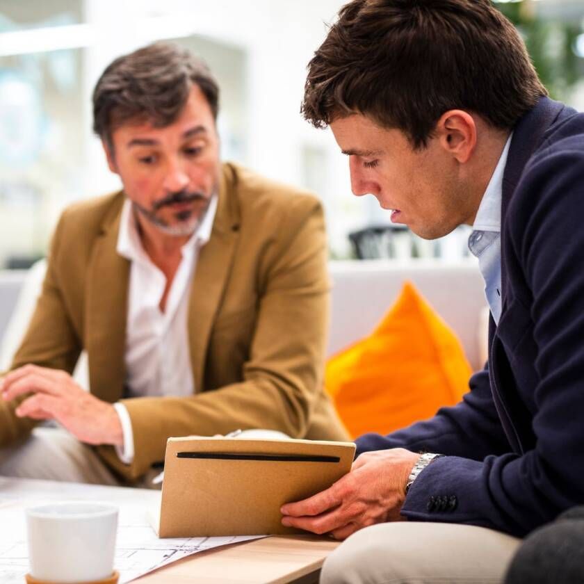 Two coworkers discussing a tablet at a table in a bright office lounge.
