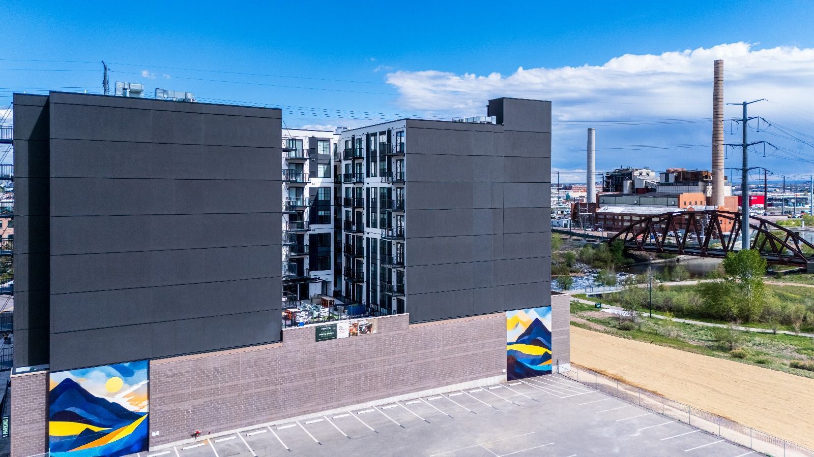 Modern apartment building with colorful mural; in the background are power lines and industrial structures.