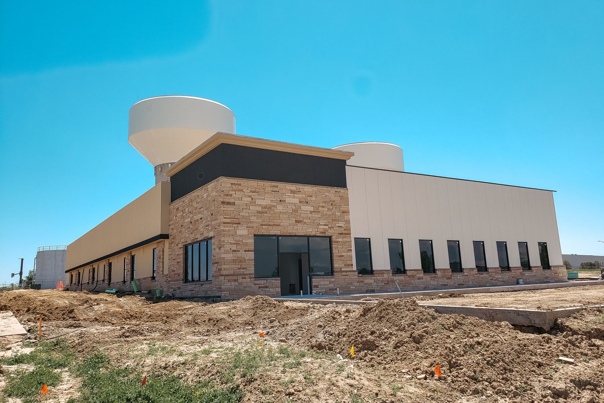 Building under construction with beige walls, stone accents, and a water tower against a blue sky.