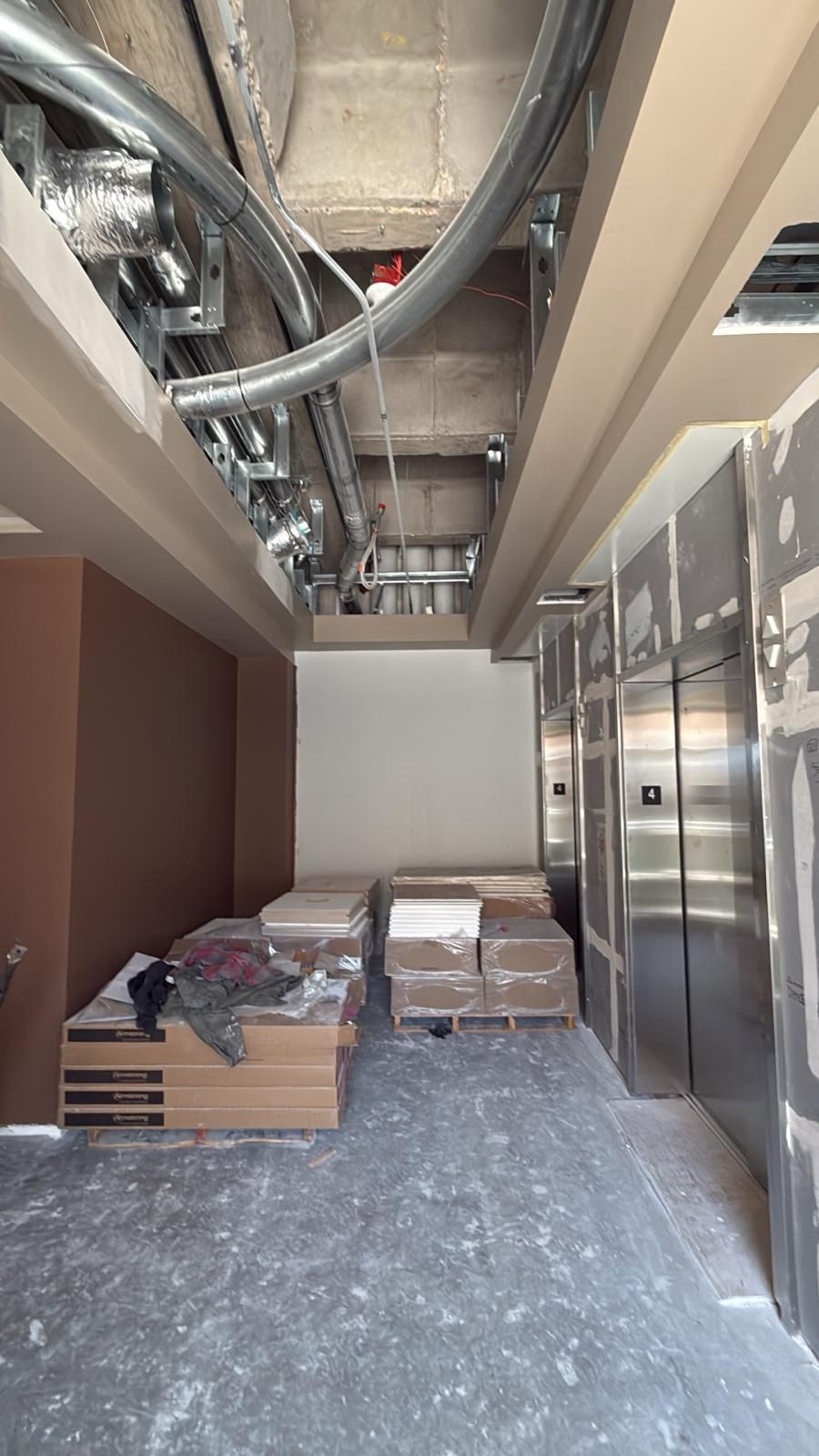 Construction site: unfinished elevator lobby with ductwork, boxes, and elevators.