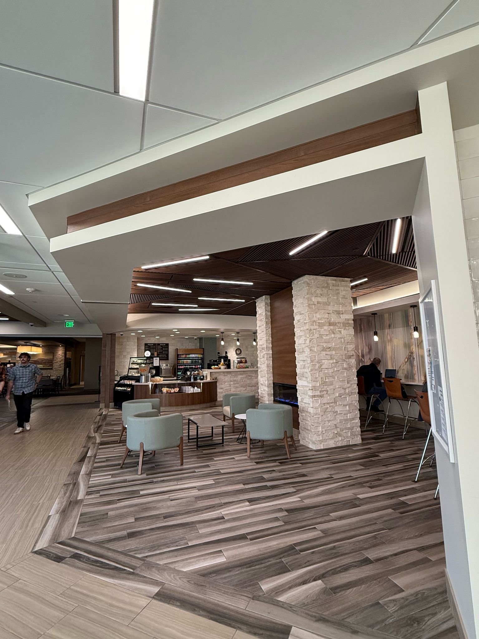 Lobby seating area with patterned carpet, chairs, and stone column. Person walks past.