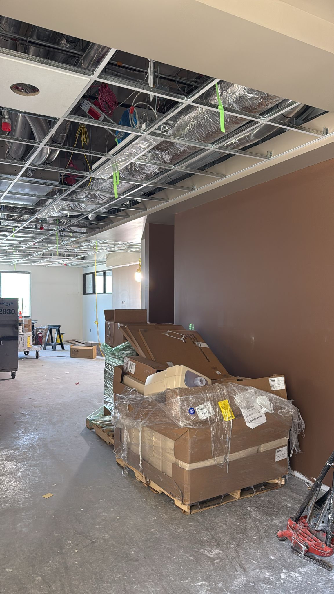 Construction site interior; exposed ceiling grid, boxes of materials stacked near a brown wall.