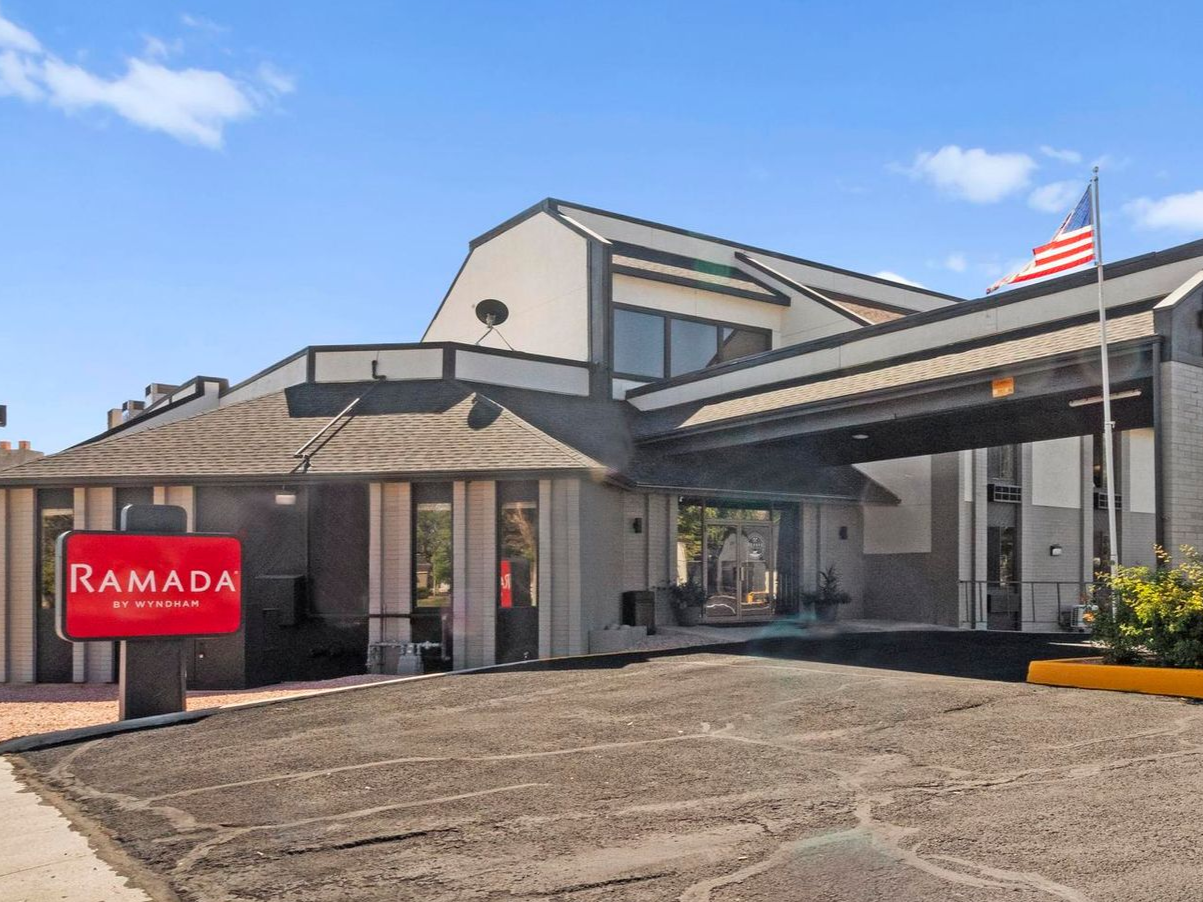Ramada hotel exterior with a covered entrance, red sign, and American flag.