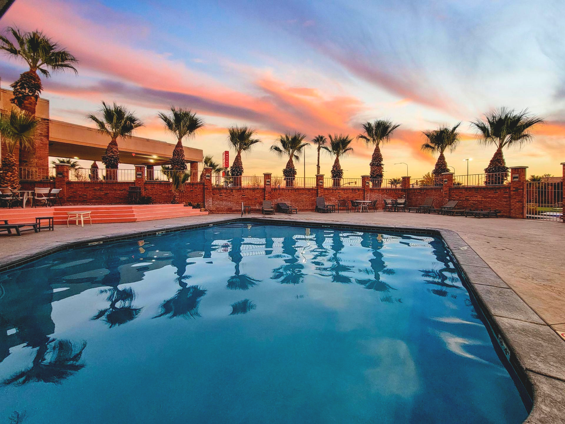 Pool with palm trees, brick wall, and sunset sky in the background.