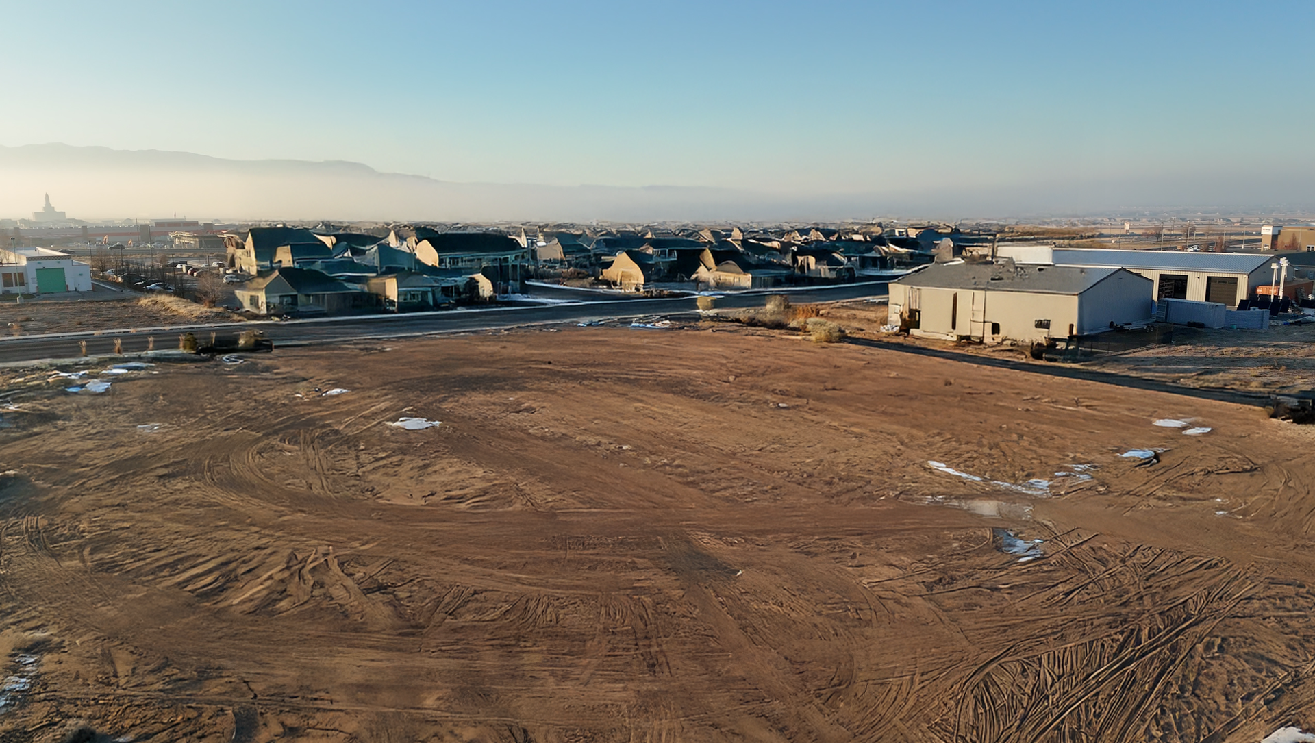 A barren field with scattered buildings and houses in the background on a sunny day.