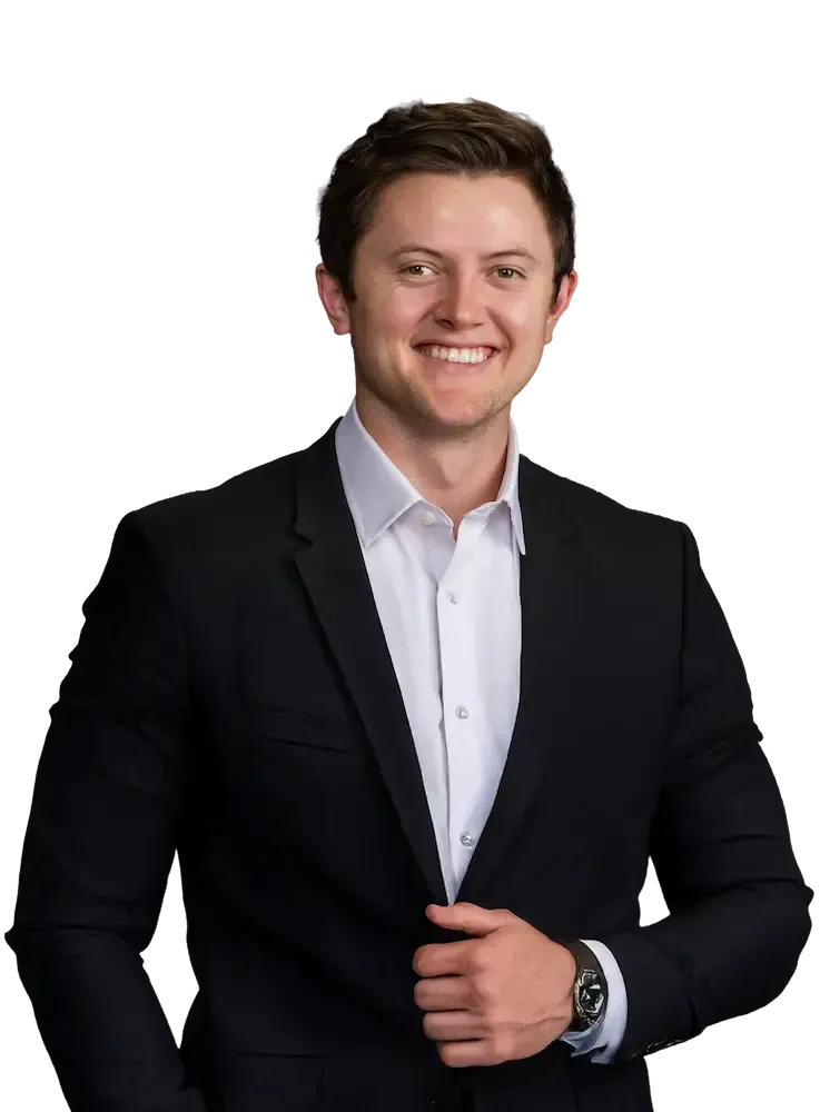 Parker Paulsen in a suit smiling, looking at the viewer. He is against a tansparent background.