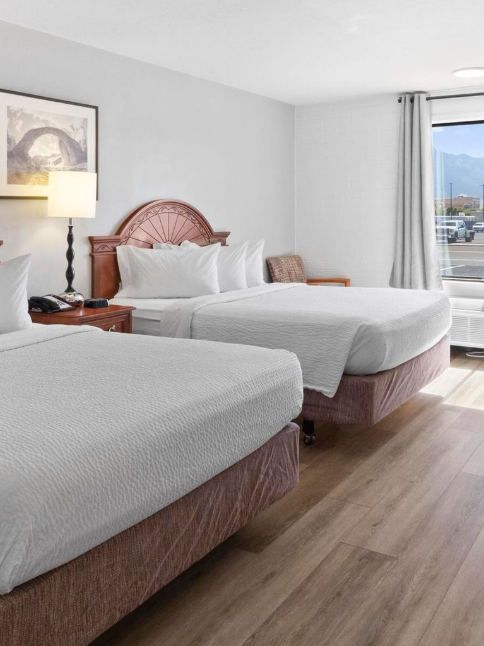 Hotel room with two queen beds, a lamp, and a window with a view.