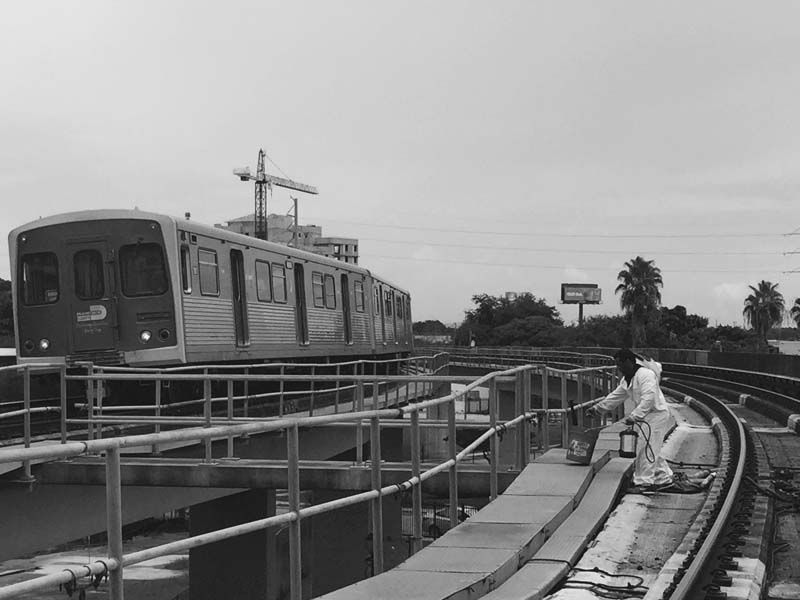 Monochrome train on elevated track. Person with lamp near track. Outdoor setting.