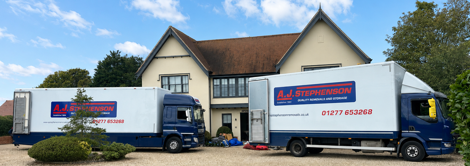 Two white delivery trucks parked outside a house with a red-tiled roof