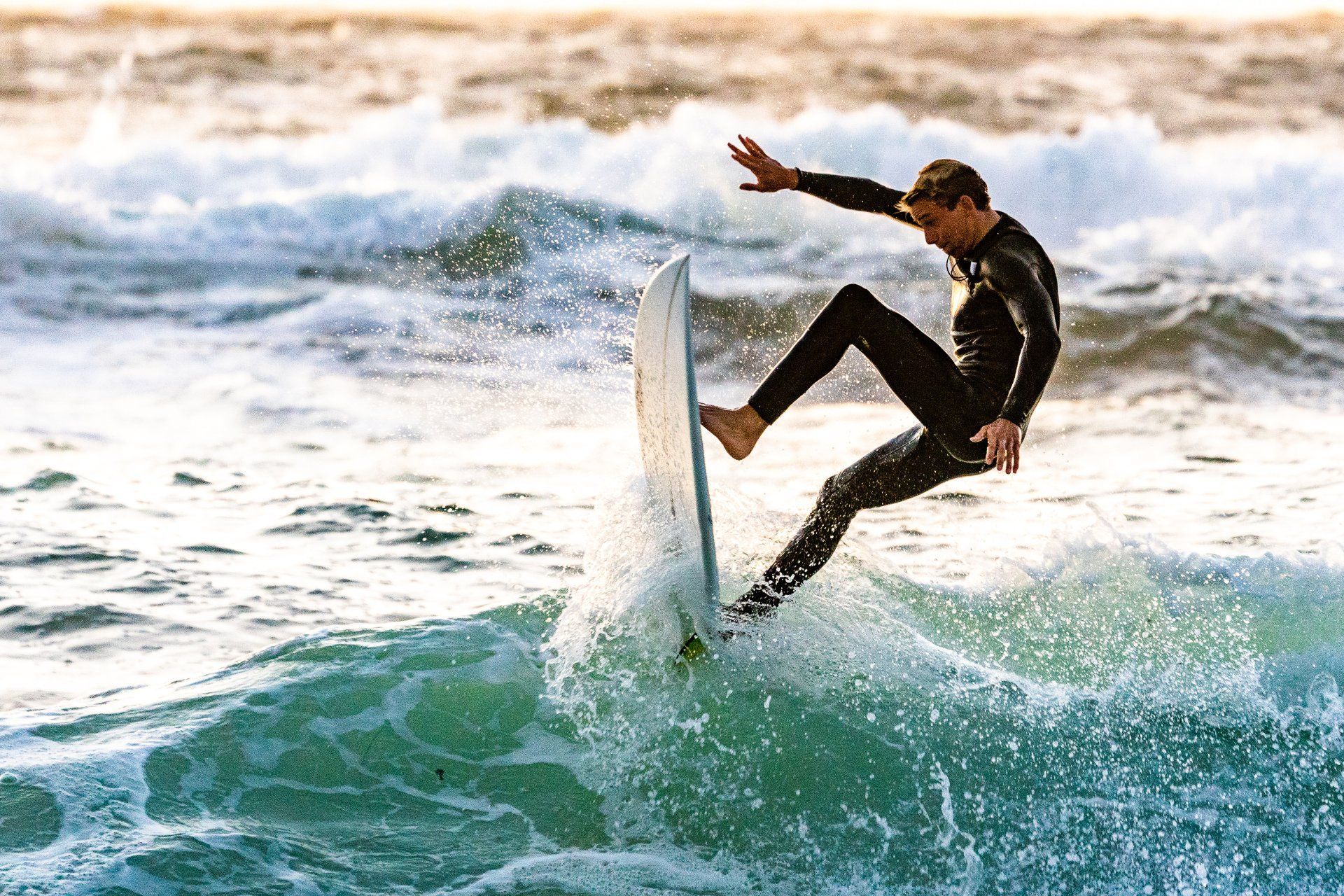 Surfer mid-air on a wave, balancing on a white surfboard in choppy blue water.
