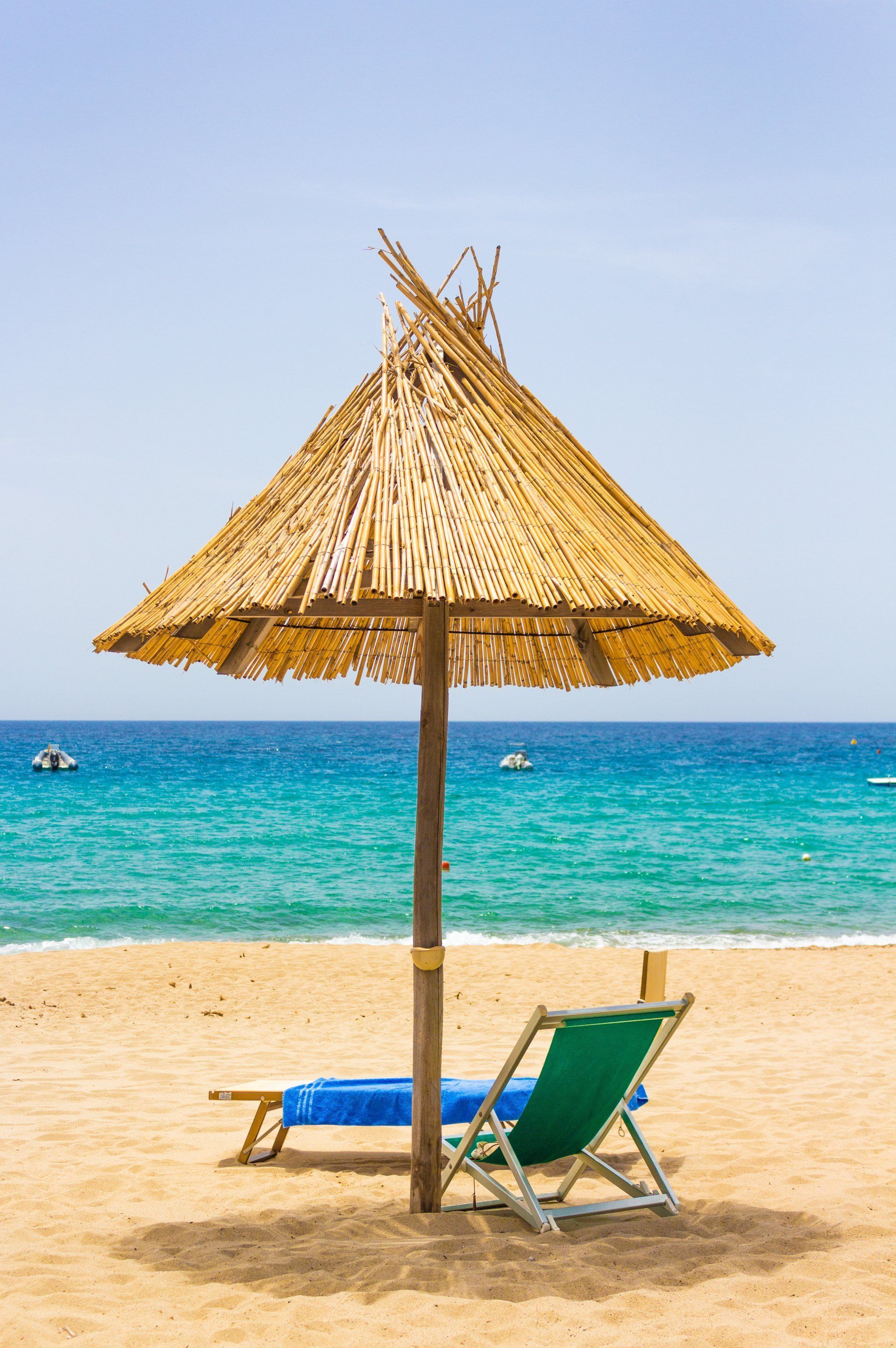Beach chair under a straw umbrella on a sandy shore beside turquoise sea and blue sky