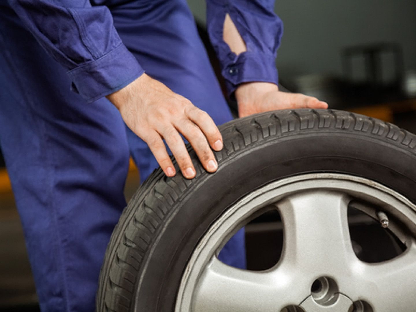 Mechanic in blue coveralls inspecting a car tire and wheel