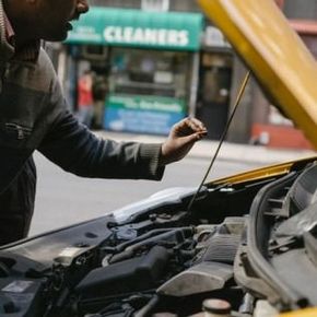 Person inspecting a car engine with the hood open on a city street