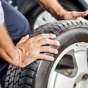Hands changing a car tire on a silver wheel outdoors.
