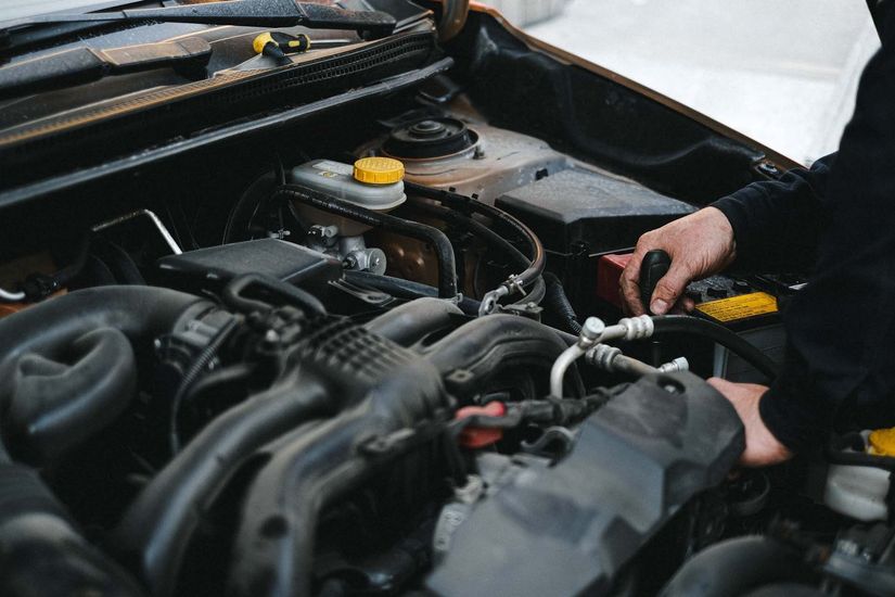 Person working on a car engine in an open hood, using tools in the engine bay.