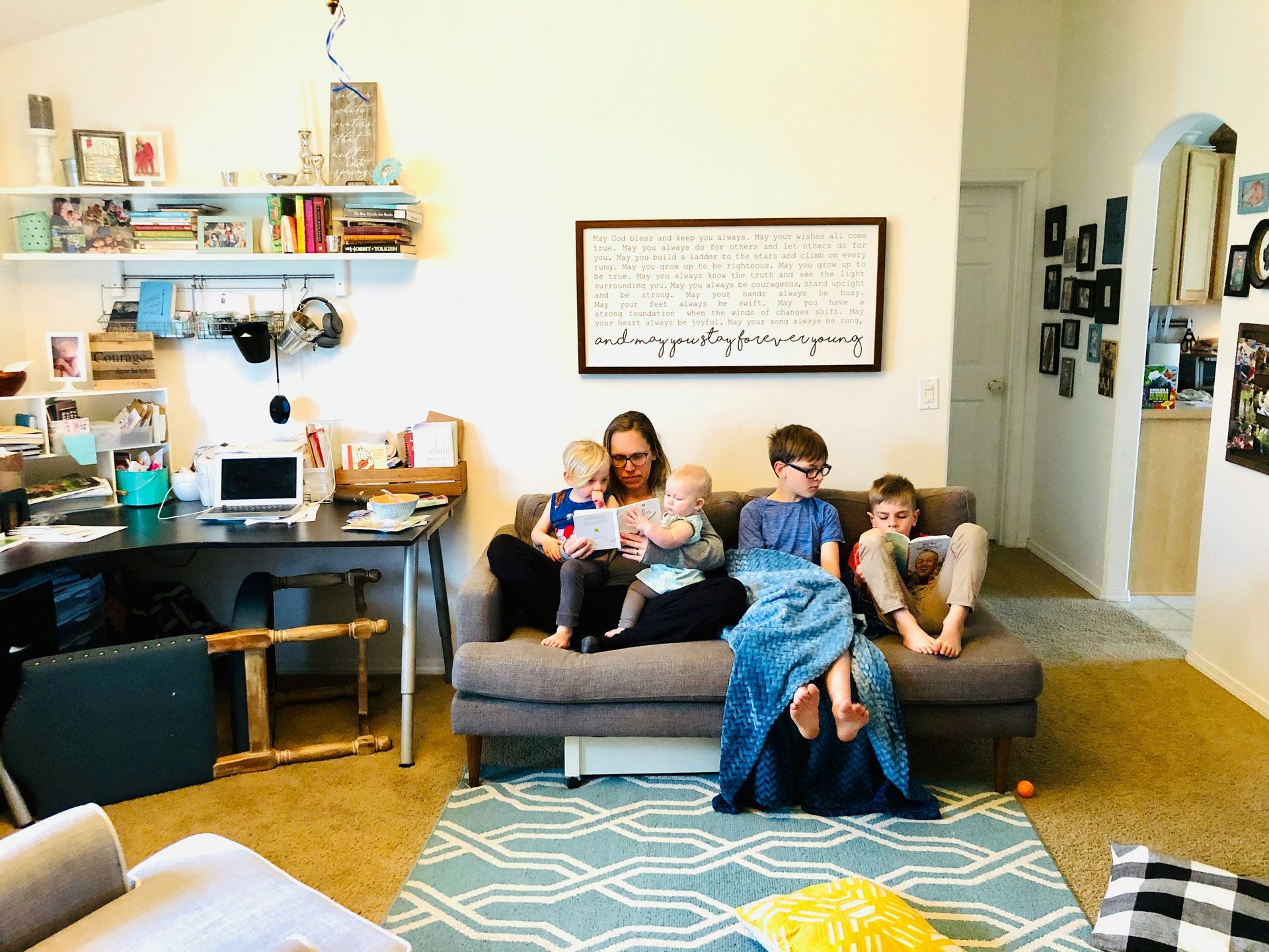 Woman and three children on a couch, reading and using tablets in a living room.