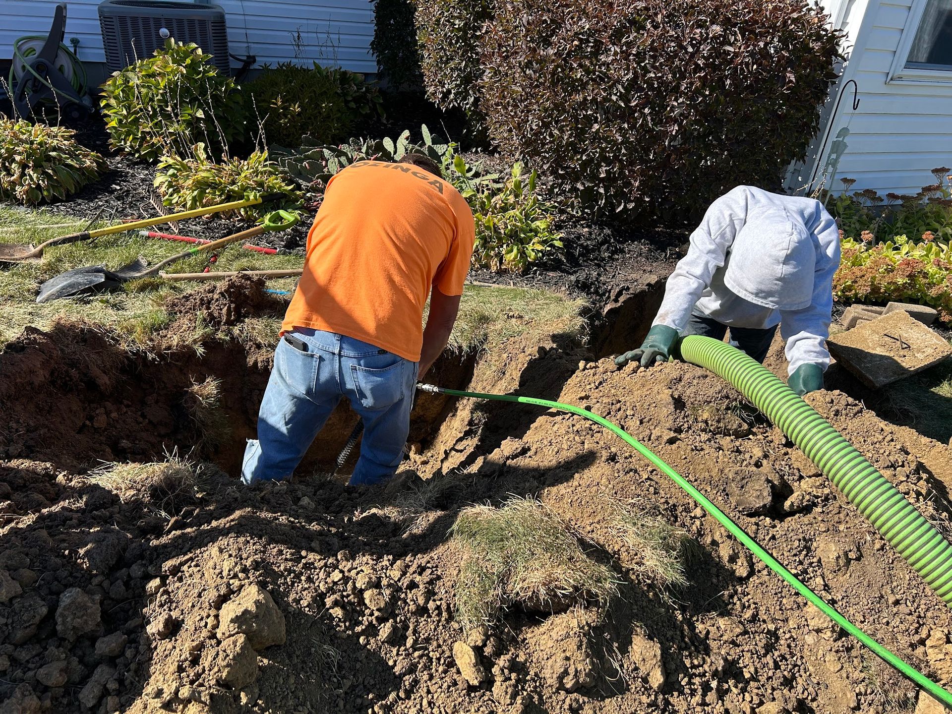 Two men are working in the dirt in front of a house.