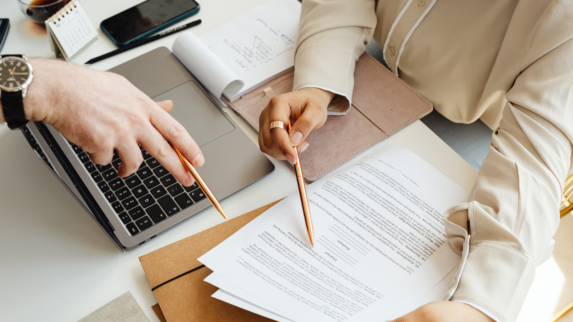 Hands in white sleeves reviewing a document with a pen at a desk.