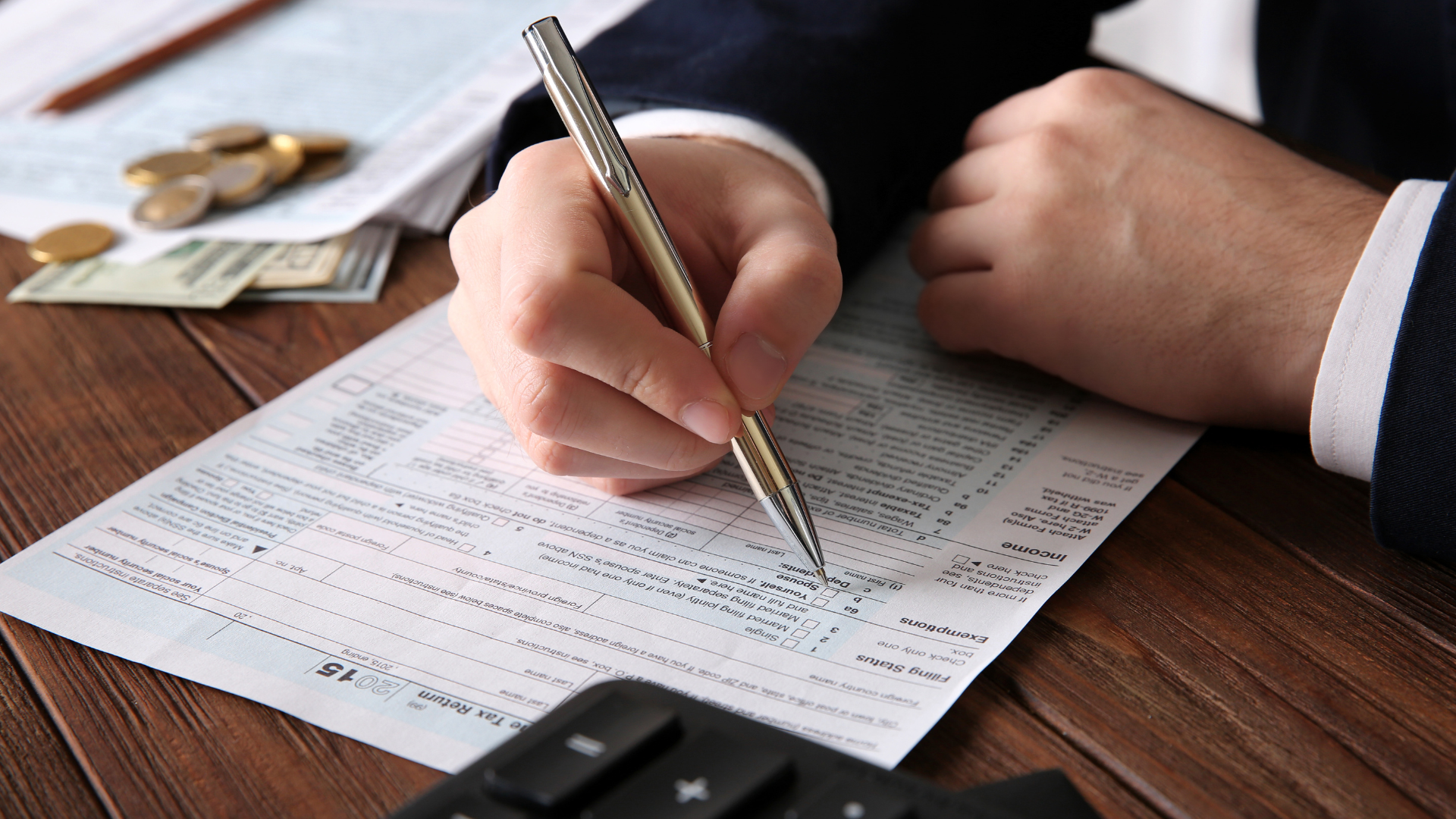 Hands signing a document on a wooden table with stacked papers in the foreground