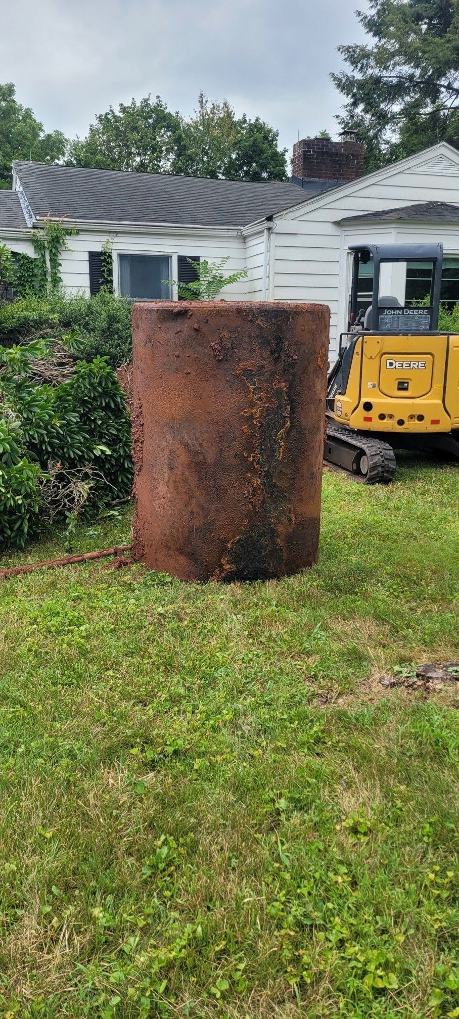 Rusty, cylindrical tank sits in a grassy yard. A small bulldozer is behind the tank, a house in the background.