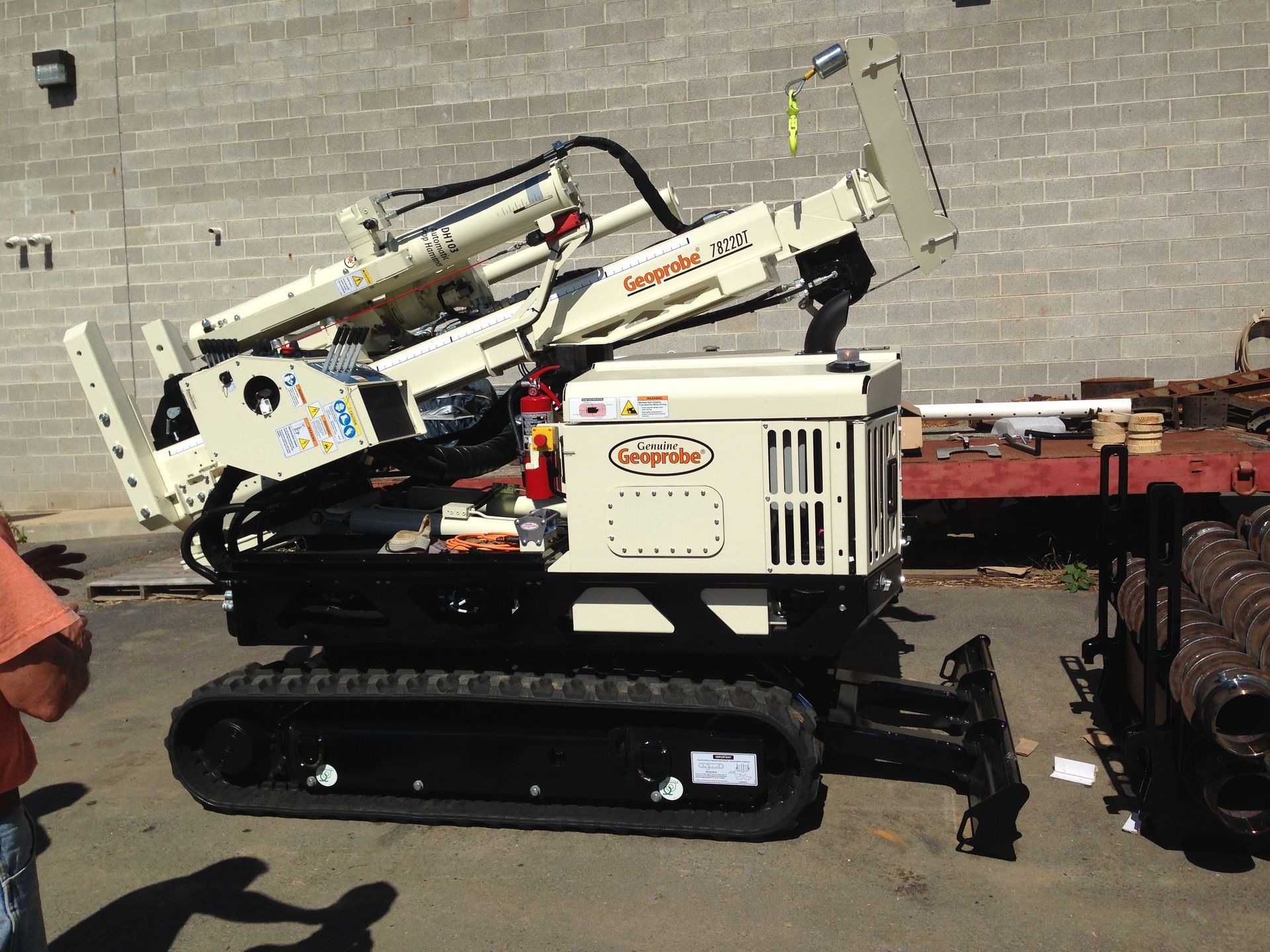 Tan and black Ditch Witch directional drill on tracks in front of a concrete block wall.