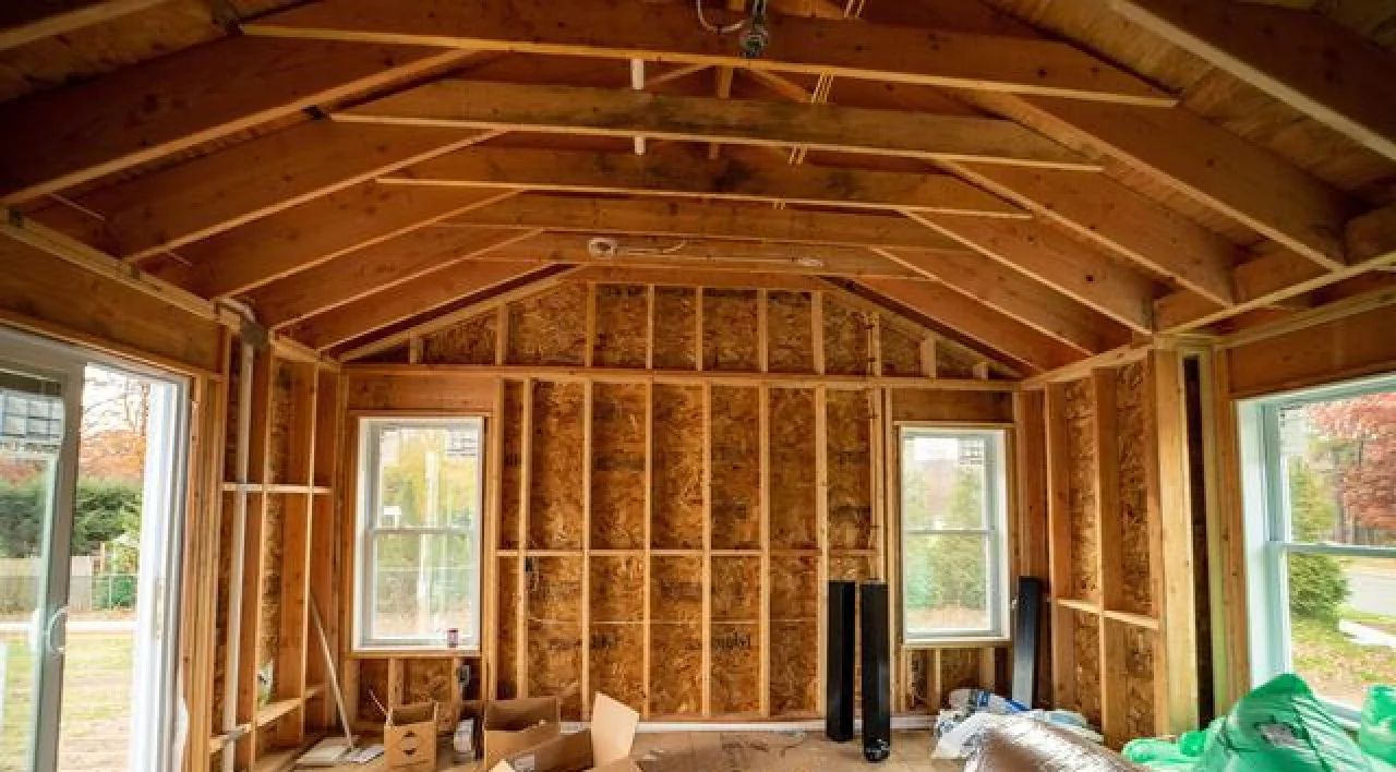 Interior of a wooden-framed house under construction with exposed insulation and windows on both sides