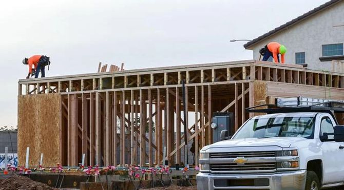 Workers framing a house addition beside a white pickup truck.