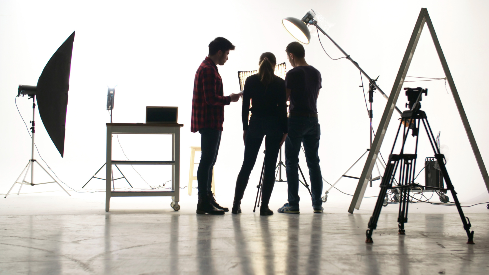 Studio crew talking beside lighting equipment and camera tripod on a white seamless set