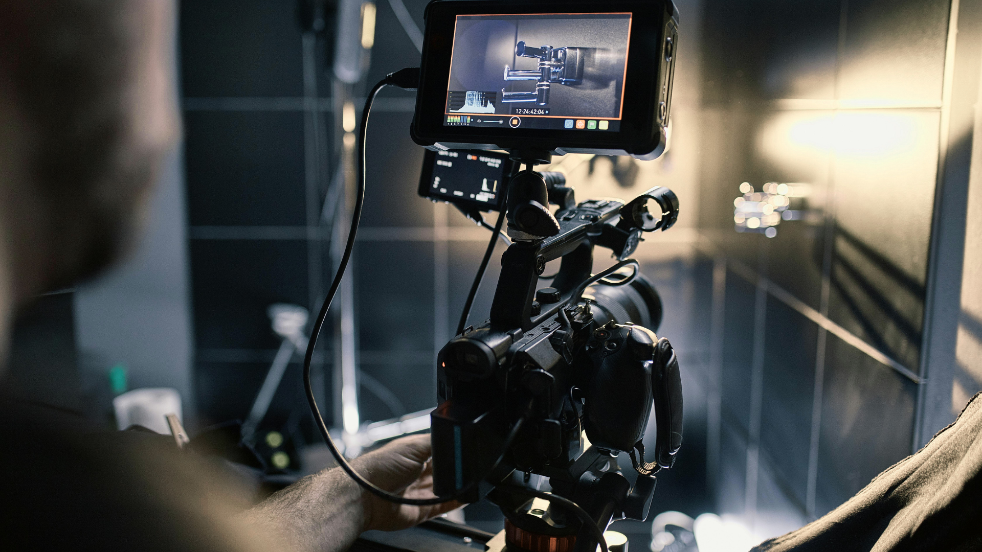 Camera setup filming a scene, with a monitor and lights in a dim studio environment