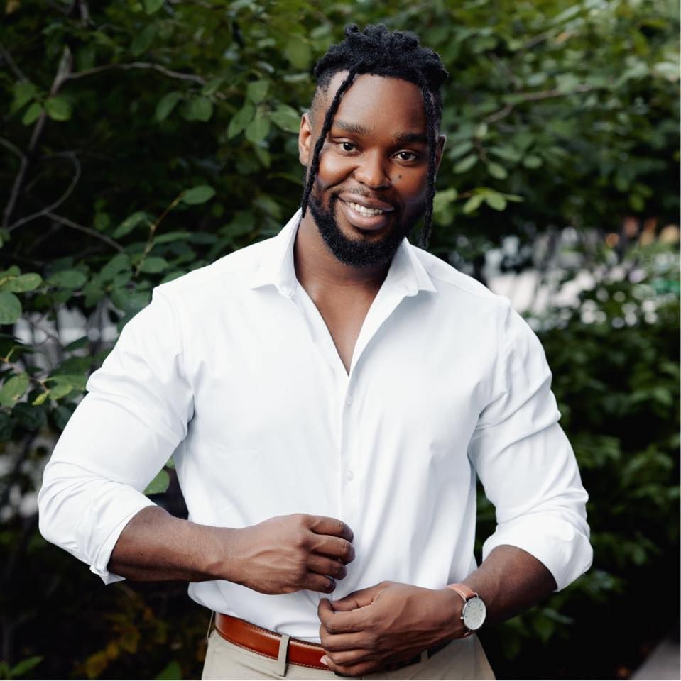 A man with a beard is wearing a white shirt and khaki pants.