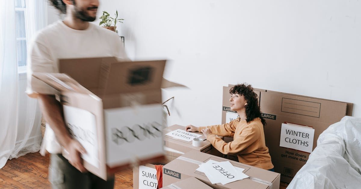 A man is carrying a box while a woman sits at a table with boxes.