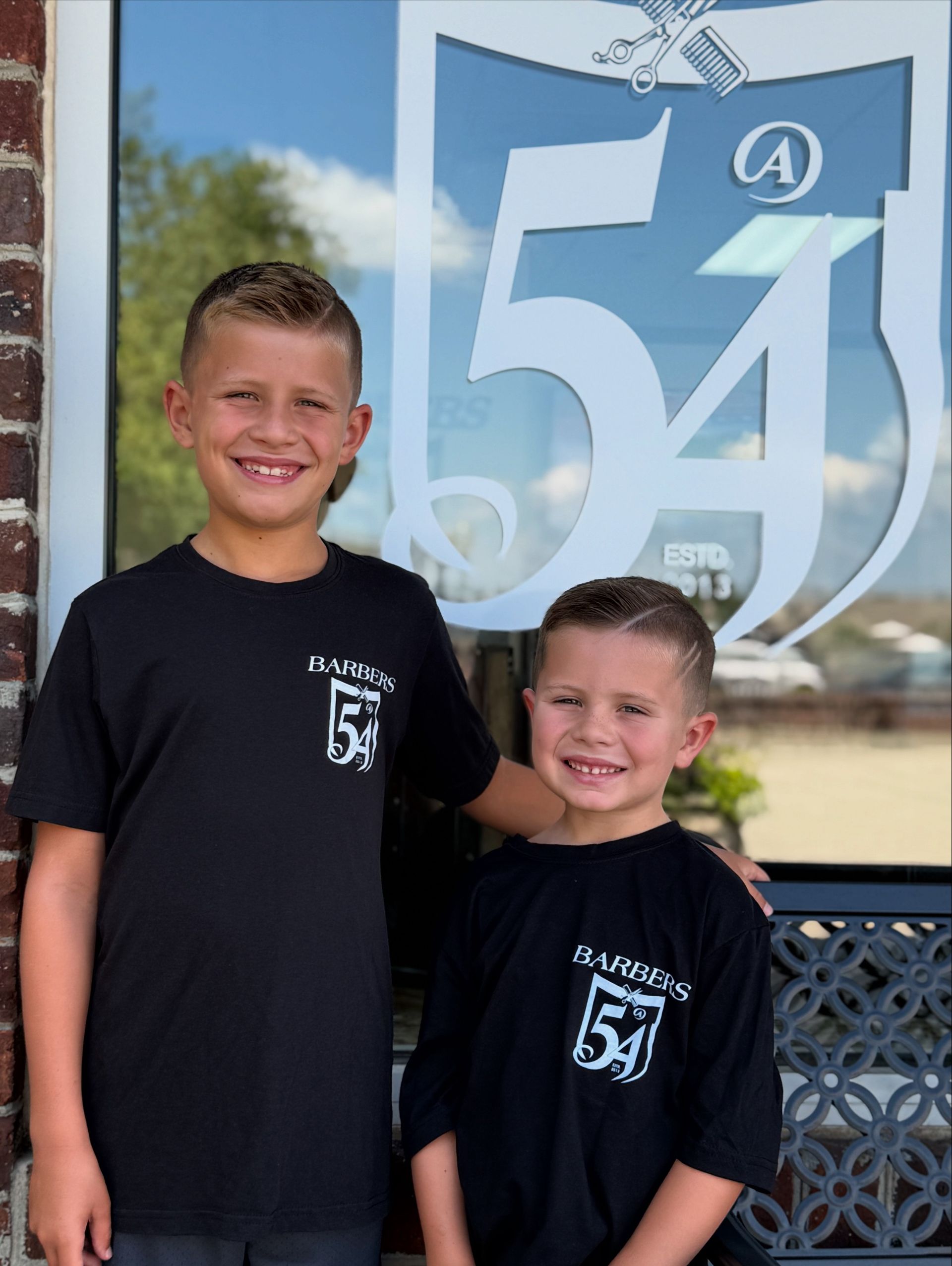 Two boys in black t-shirts in front of a window with a 