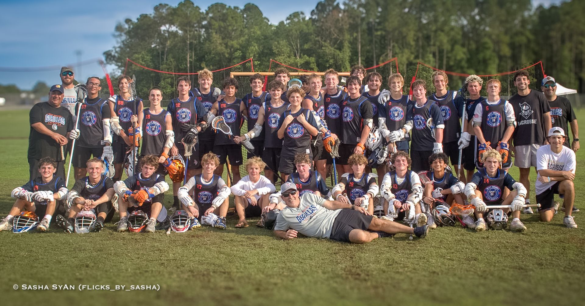 Large sports team group photo outdoors in navy uniforms on a grassy field with trees in the background