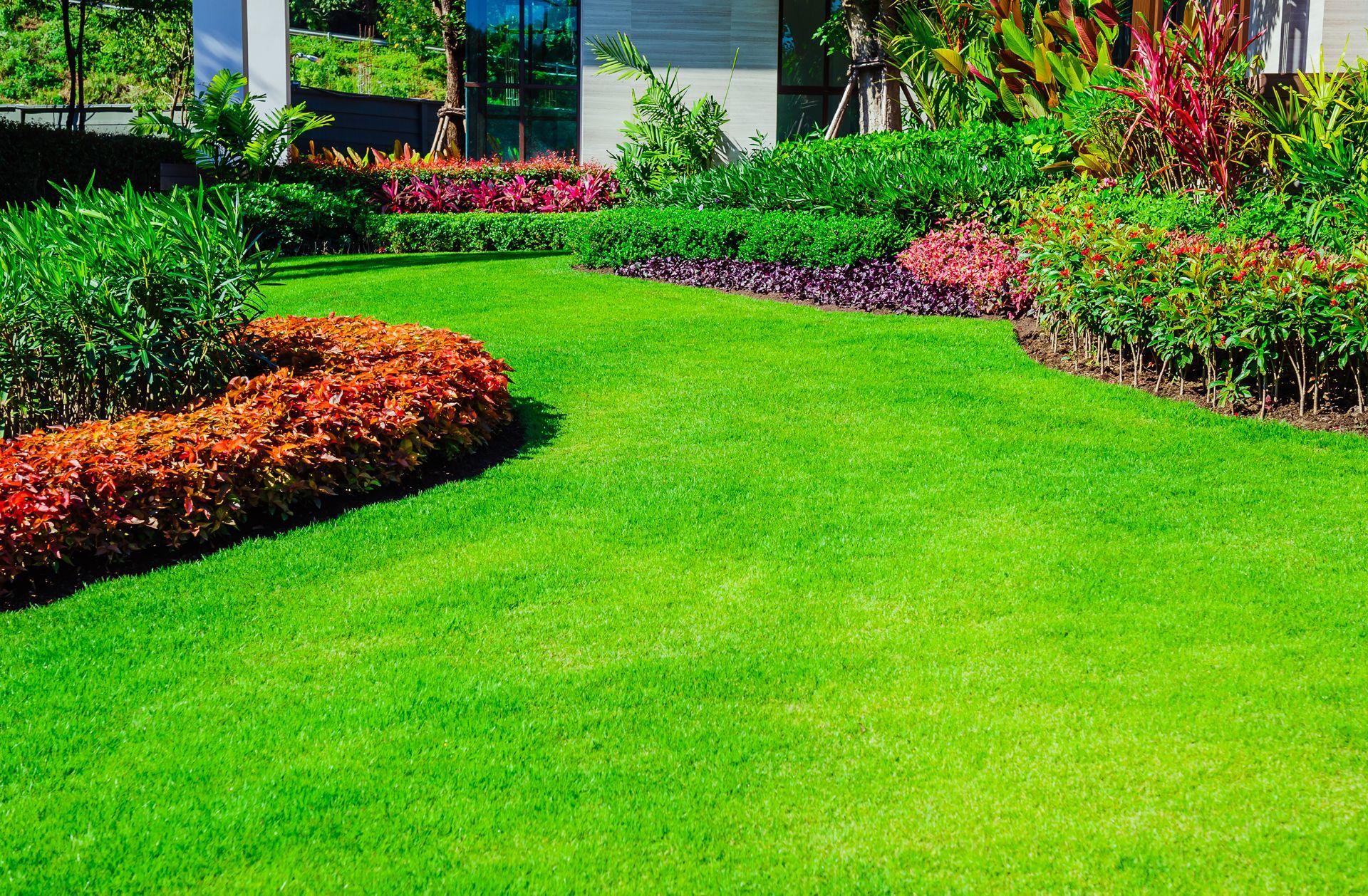 A lush green lawn with flowers and bushes in front of a house.