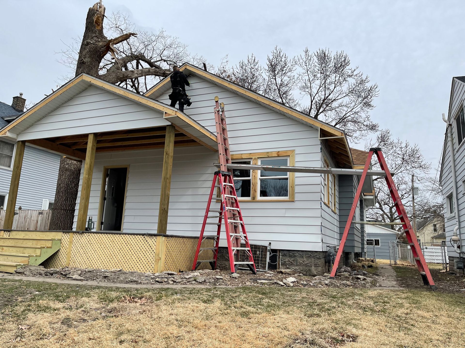 House under construction; worker on roof, ladders, scaffolding, and porch.