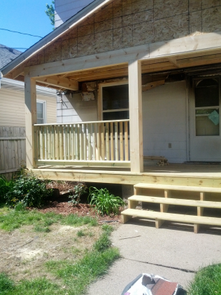 Newly constructed wooden porch with railing, steps, and posts. The house exterior is visible.