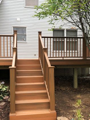 Wooden deck with stairs leading to a house. Brown railing and steps. Gray siding.