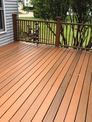 Wooden deck with brown railing, next to a gray house, overlooking green yard.