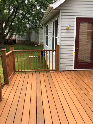 Wooden deck with railing, connected to a light-colored house with a dark red door and windows.
