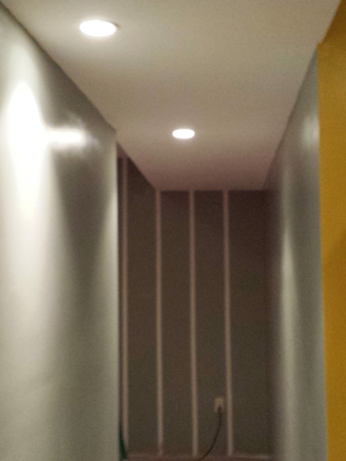 Narrow hallway with recessed ceiling lights and partially constructed wall.