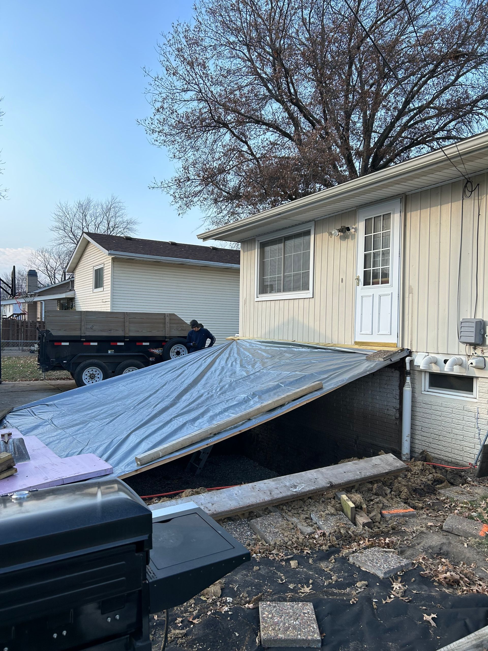 Exterior of a building with a tarp-covered entrance ramp. A dumpster truck is parked nearby.