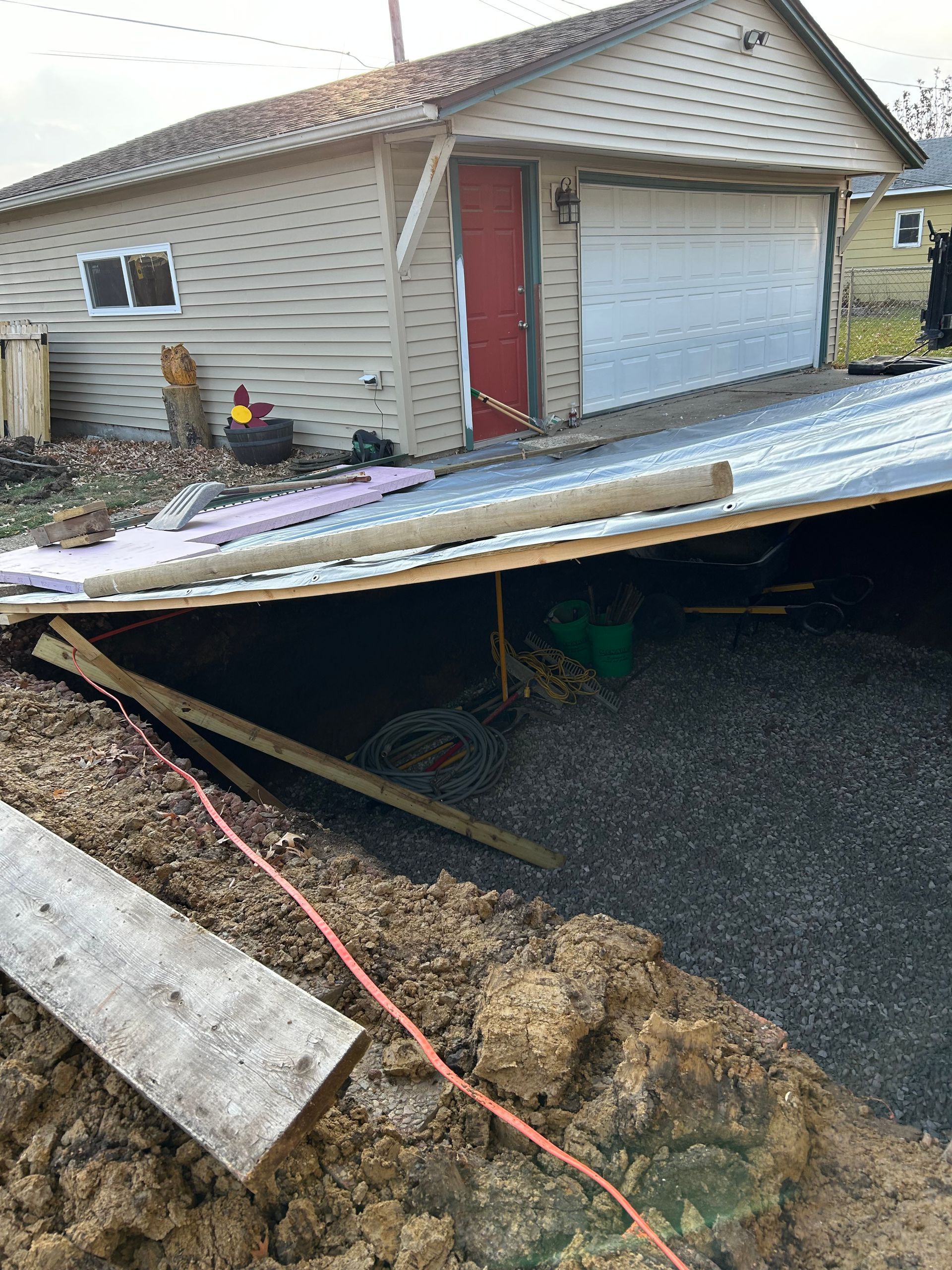 A collapsed shed roof over a pile of gravel, next to a beige garage with a red door.
