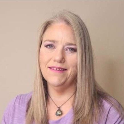 A woman wearing a purple shirt and a necklace is smiling for the camera.