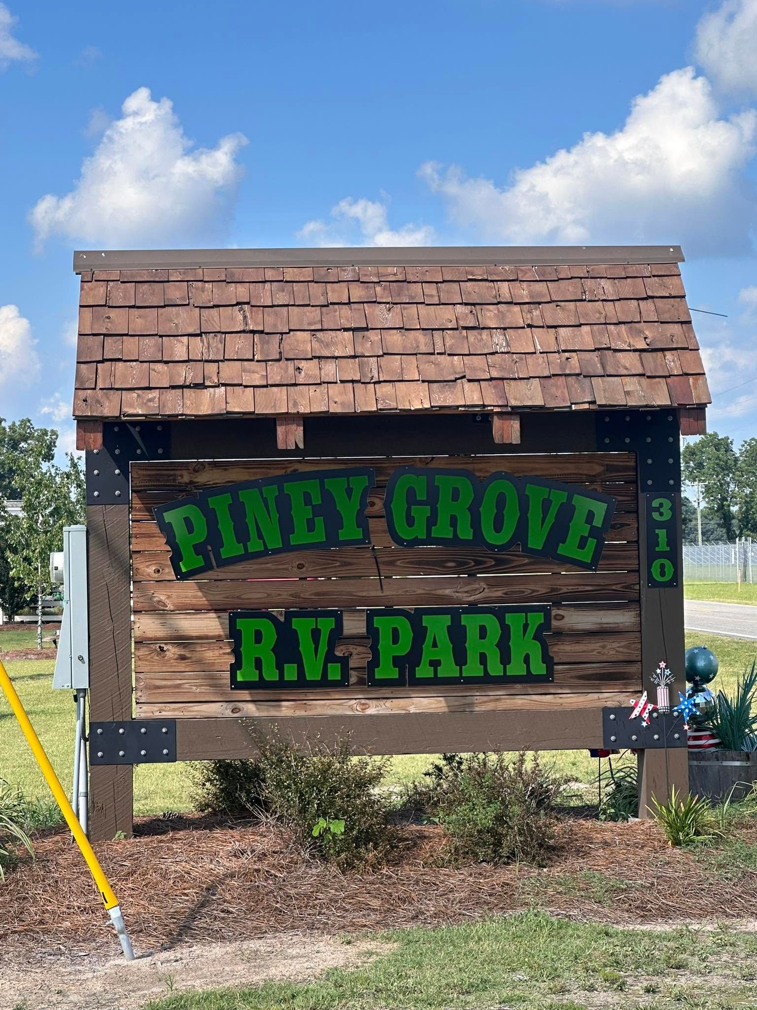 Piney Grove RV Park sign on a wooden structure under a blue sky with clouds.