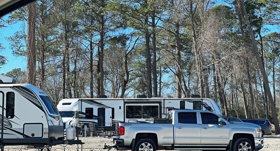 Several parked RVs and pickup trucks in a wooded campground under a clear sky