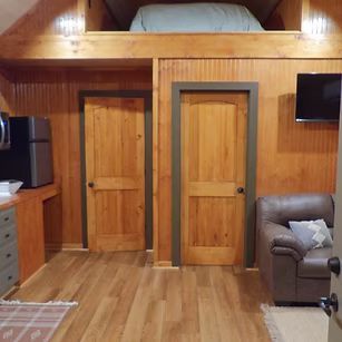 Small loft bedroom with wood walls, two wooden doors, bed nook above, and a couch at right.