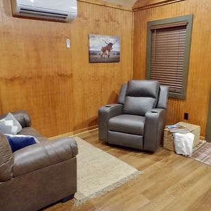 Cozy wood-paneled living room with two recliners, a sofa, rug, window blinds, and wall-mounted air conditioner