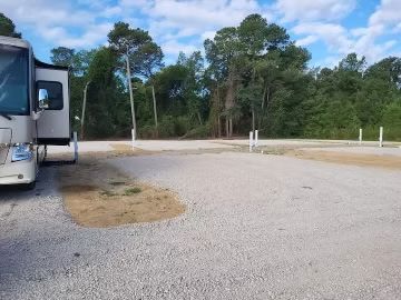 RV parked beside a gravel lot with trees and a wooded campsite in the background
