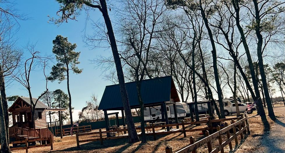 Wooded park with cabins, a blue-roofed pavilion, and a wooden walkway in winter light