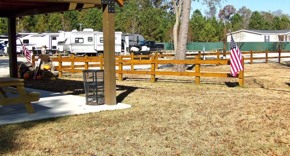 Wooden fence with an American flag beside a pavilion in a sunny park or campground.